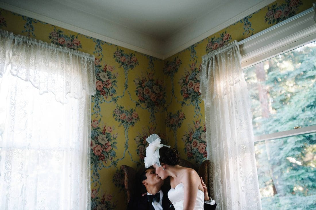 fun artistic shot of bride and groom kissing against floral wall paper at Atherton Wedding